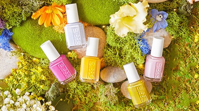 6 bottles of nail polish laid down on a mossy ground with mossy rocks and flowers