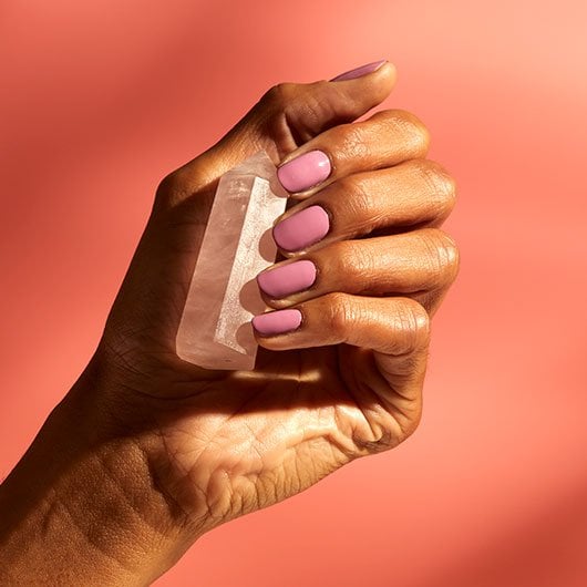 medium skin hand model holding a pink crystal wearing creamy purple breathe in, breathe out polish 