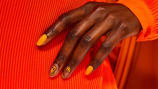 woman in orange outfit with nail polish design of melting yellow smiley faces
