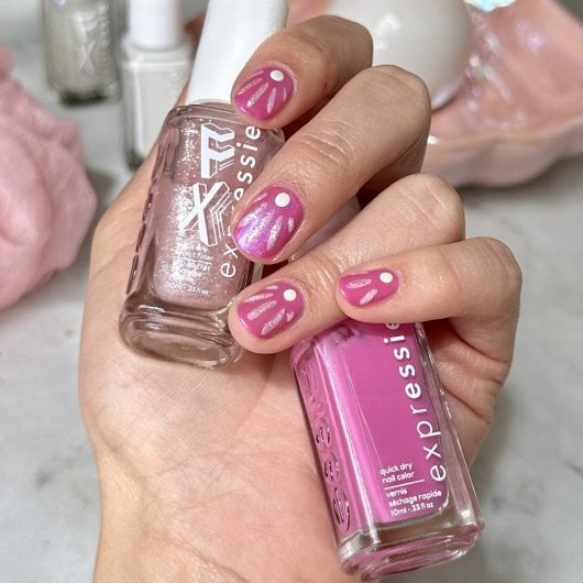 light skin hand with seashell nail art holding pink and pink shimmer nail polish bottles