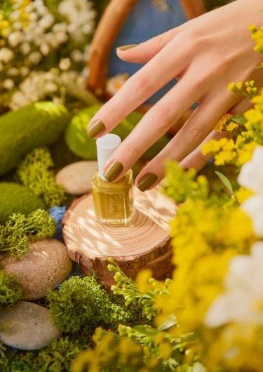 a hand with green painted nails hovering over a green essie nail polish bottle standing on wood with a moss background