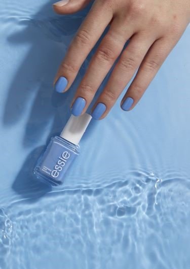 a hand with blue painted nails hovering over a blue essie nail polish bottle with blue water and waves in the background