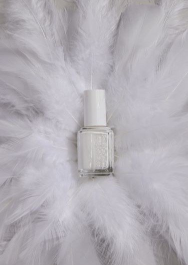 a white essie nail polish bottle laying on a bed of white feathers placed in a circle around the bottle
