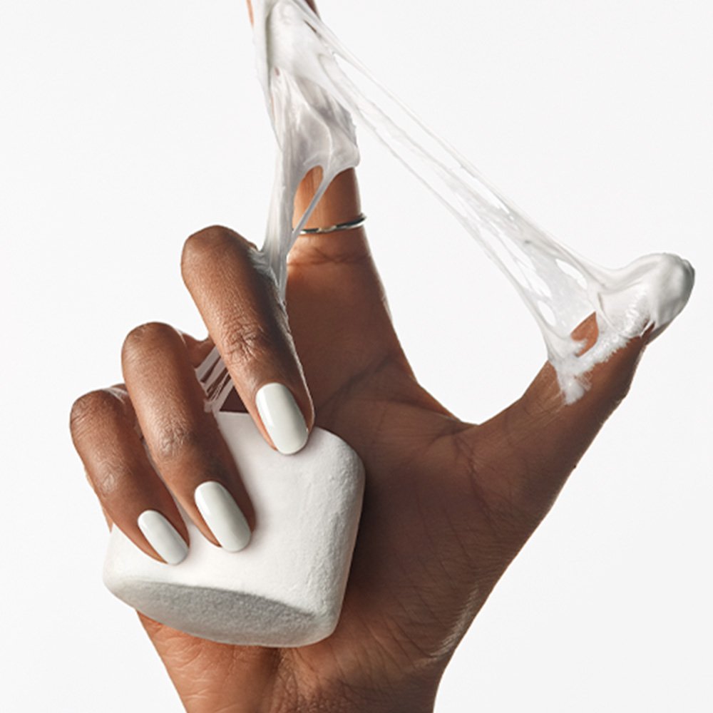 Large marshmallow in dark skin hand wearing white polish, melted goo between index finger and thumb