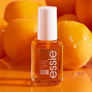 Bottle of essie apricot cuticle oil in front of pile of apricots on orange table
