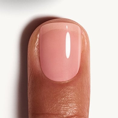Closeup of a medium skin fingertip painted in peach pink nail polish Sugar Daddy