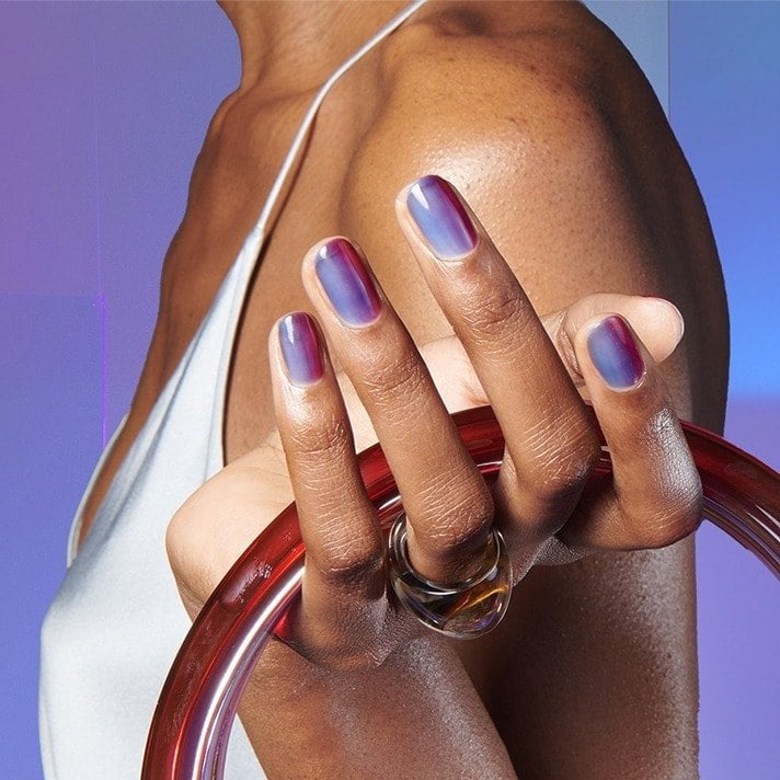 Model in white thin strap top holds a translucent red glass purse; almond nails feature violet glassy nail polish.