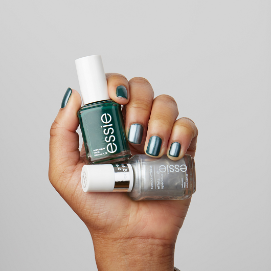 manicured hand holding bottles of off tropic and cosmic chrome against a gray background