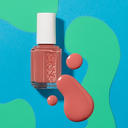 Bottle of coral nail polish and matching pools of color posed on a swirly blue and green background