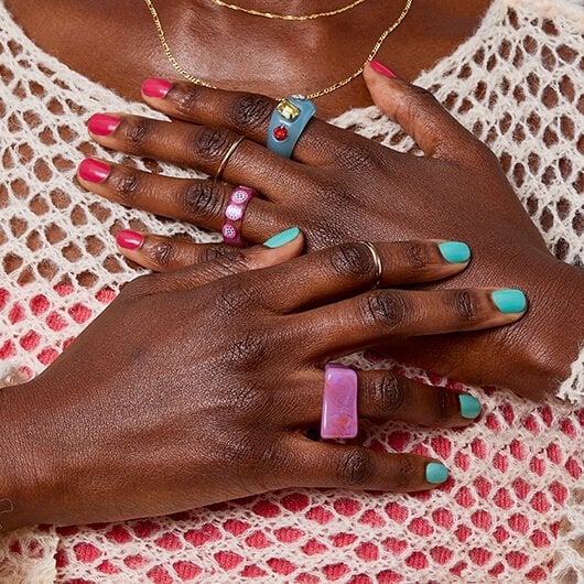 Model wearing rings with hands placed on chest and wearing a two tone pink and blue manicure