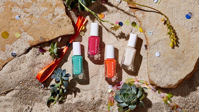 Four bottles of expressie nail polish on a rocky beach background with a wristband and succulents