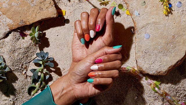Two hands painted with a colorful multi-mani against a rocky beach background