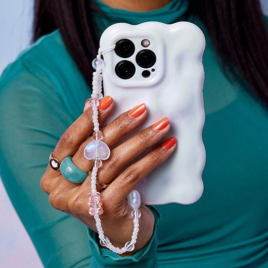 Orange manicured hand holding phone with bubbled white phone case and charm strap