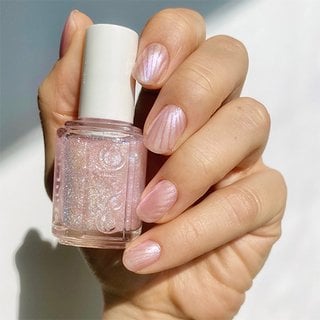 Light skin hand holding pink shimmer nail polish, nails in a seashell pearl design